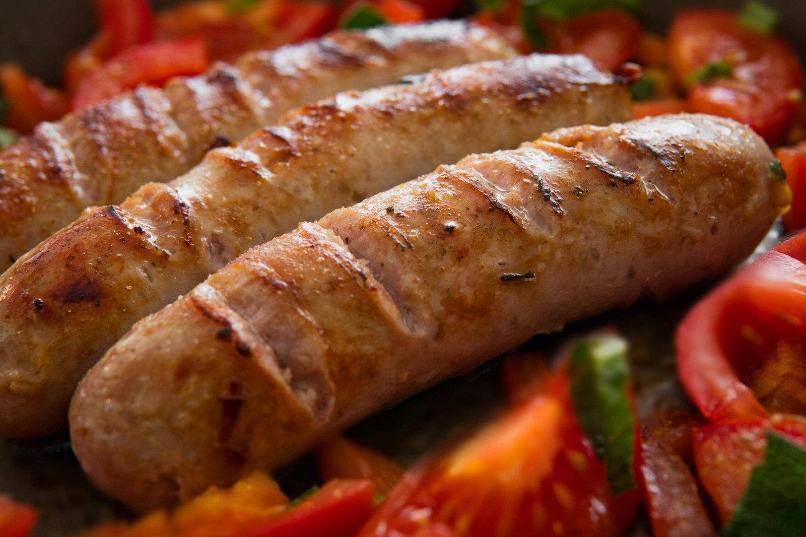 Close-up of juicy grilled sausages served with fresh sliced tomatoes.